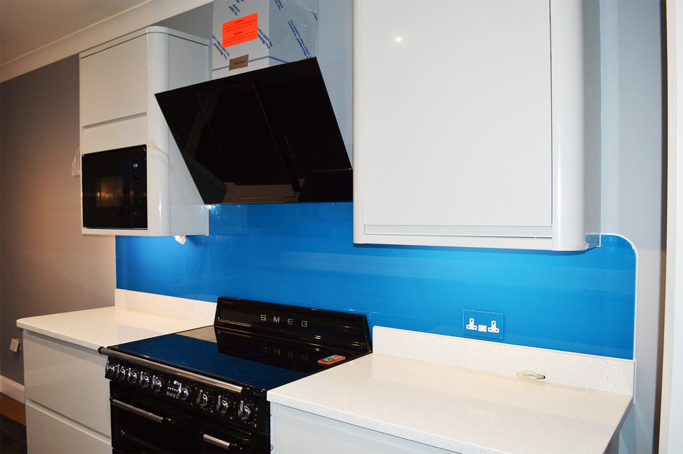 Bild på ett stort funkis kök och matrum, med släta luckor, vita skåp, bänkskiva i kvartsit, blått stänkskydd och glaspanel som stänkskydd