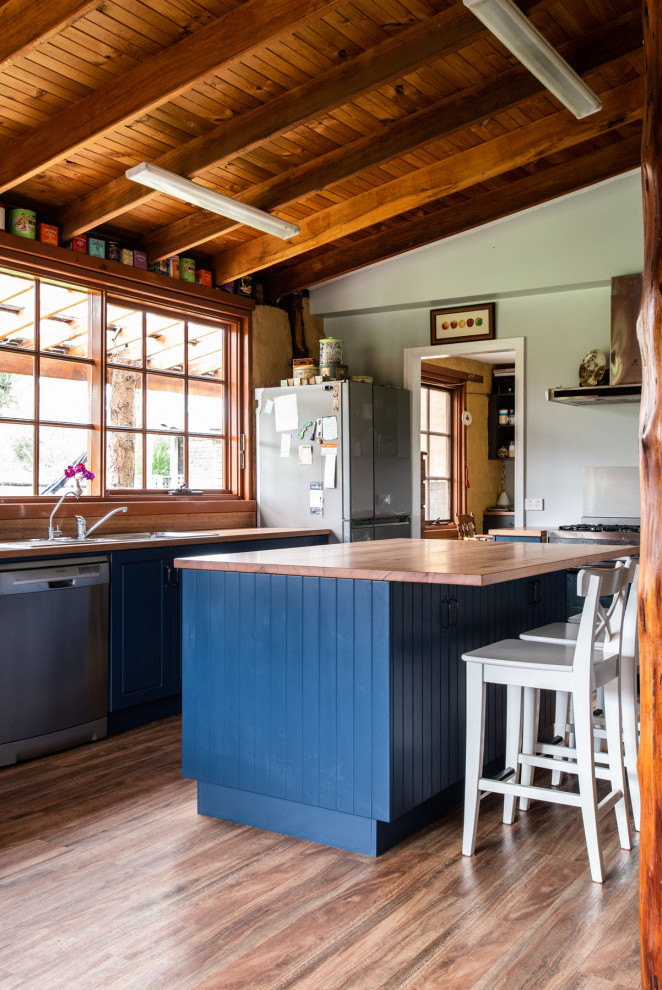 Foto de cocina rural con fregadero encastrado, puertas de armario azules, encimera de madera, electrodomésticos de acero inoxidable, suelo de madera oscura, una isla, suelo marrón y encimeras marrones