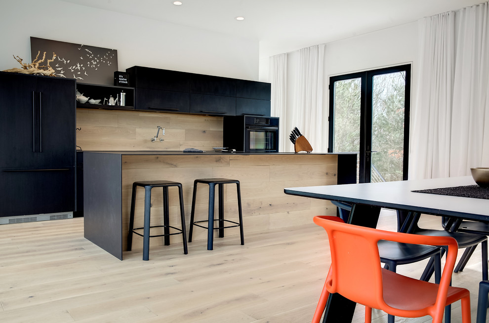 Immagine di una cucina minimalista di medie dimensioni con lavello integrato, ante lisce, ante nere, top in quarzo composito, paraspruzzi in legno, elettrodomestici neri e parquet chiaro