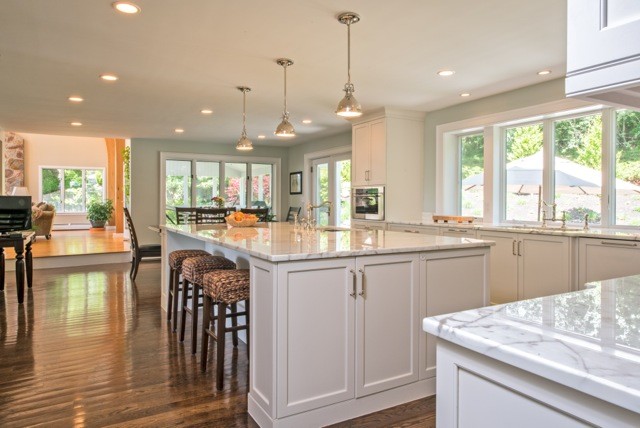 Photo of a large traditional l-shaped kitchen/diner in Boston with a submerged sink, recessed-panel cabinets, white cabinets, stainless steel appliances, dark hardwood flooring and an island.