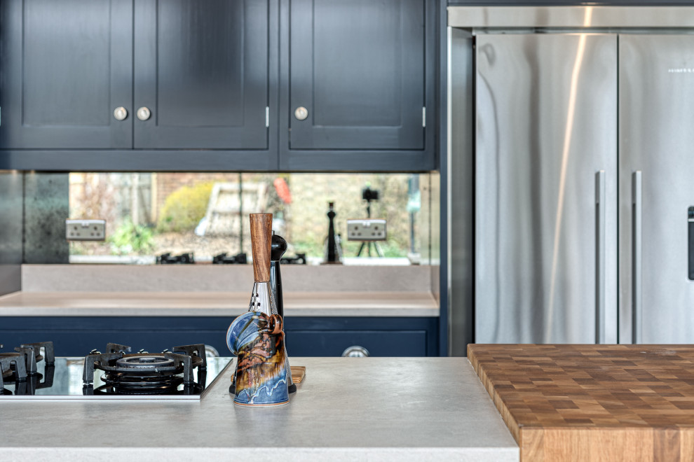 Modern inredning av ett stort grå grått kök, med skåp i shakerstil, blå skåp, bänkskiva i betong, spegel som stänkskydd, rostfria vitvaror, mellanmörkt trägolv och en köksö
