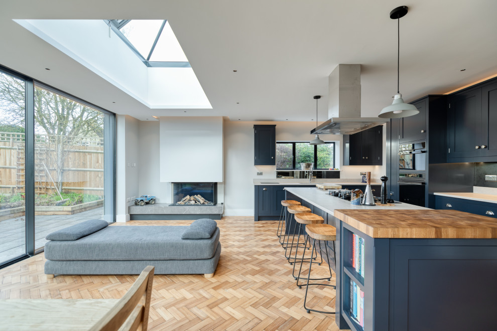 Foto på ett stort funkis grå kök, med skåp i shakerstil, blå skåp, bänkskiva i betong, spegel som stänkskydd, rostfria vitvaror, mellanmörkt trägolv och en köksö