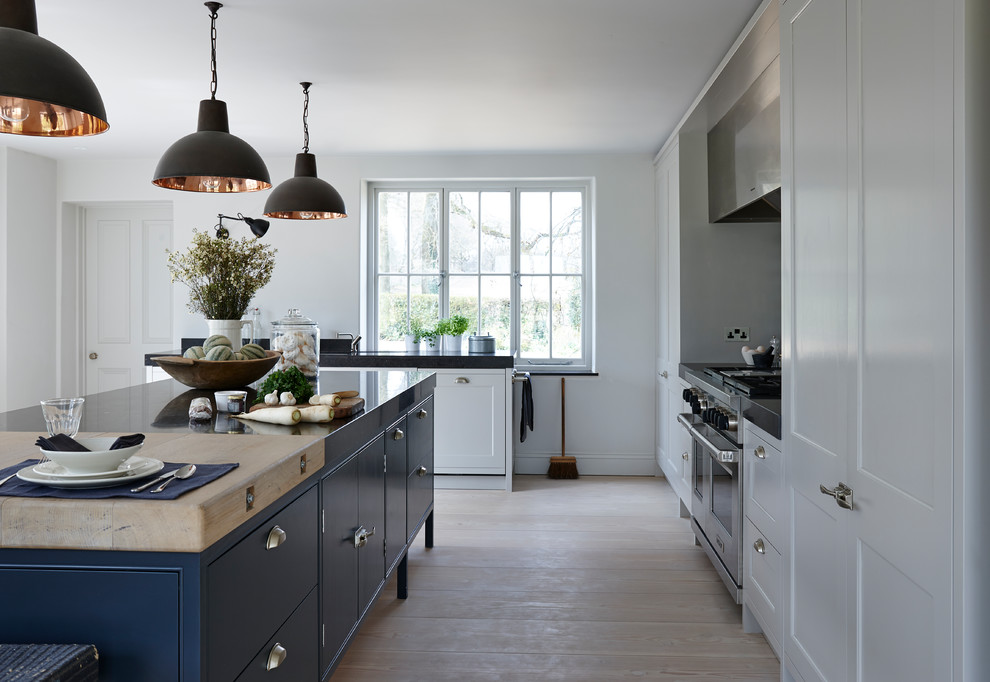 Inspiration for a medium sized rustic galley open plan kitchen in London with an integrated sink, flat-panel cabinets, blue cabinets, marble worktops, metallic splashback, mirror splashback, stainless steel appliances, light hardwood flooring, an island, brown floors and black worktops.