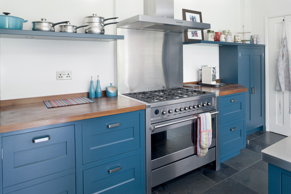 Modern inredning av ett mellanstort kök, med en integrerad diskho, skåp i shakerstil, blå skåp, träbänkskiva, stänkskydd med metallisk yta, rostfria vitvaror, skiffergolv och en köksö