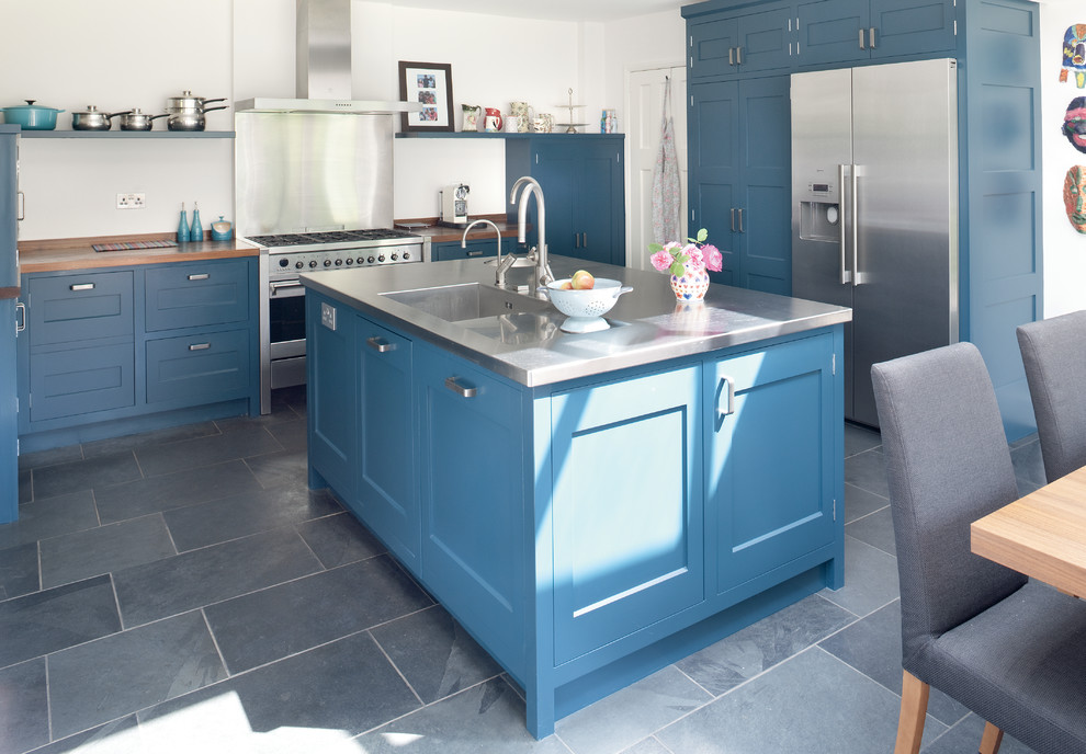 Bild på ett mellanstort funkis kök, med en integrerad diskho, skåp i shakerstil, blå skåp, bänkskiva i rostfritt stål, stänkskydd med metallisk yta, rostfria vitvaror, skiffergolv och en köksö
