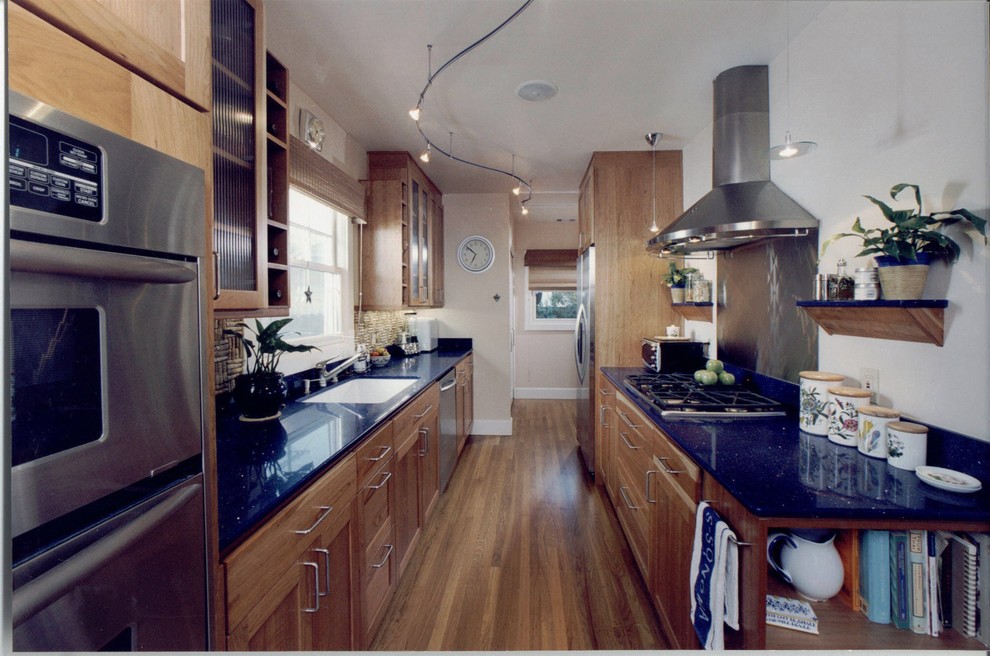 Idéer för mellanstora funkis blått kök, med en nedsänkt diskho, luckor med infälld panel, skåp i mellenmörkt trä, rostfria vitvaror, mellanmörkt trägolv, bänkskiva i kvarts, stänkskydd med metallisk yta och stänkskydd i metallkakel