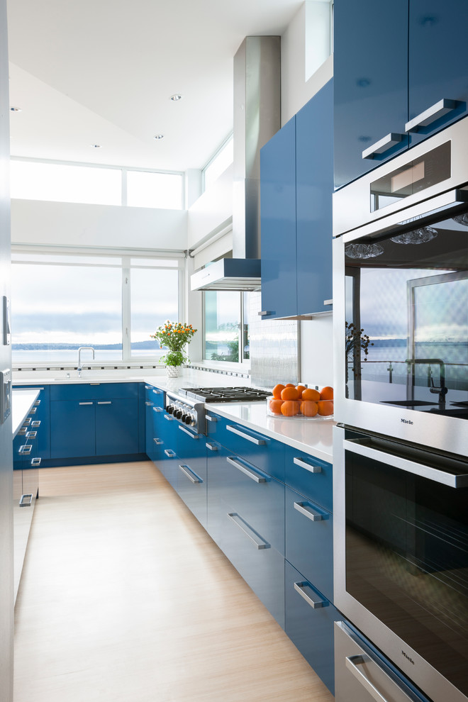 Inspiration for a mid-sized contemporary u-shaped light wood floor and beige floor open concept kitchen remodel in Seattle with an undermount sink, flat-panel cabinets, blue cabinets, solid surface countertops, metallic backsplash, metal backsplash, stainless steel appliances and an island