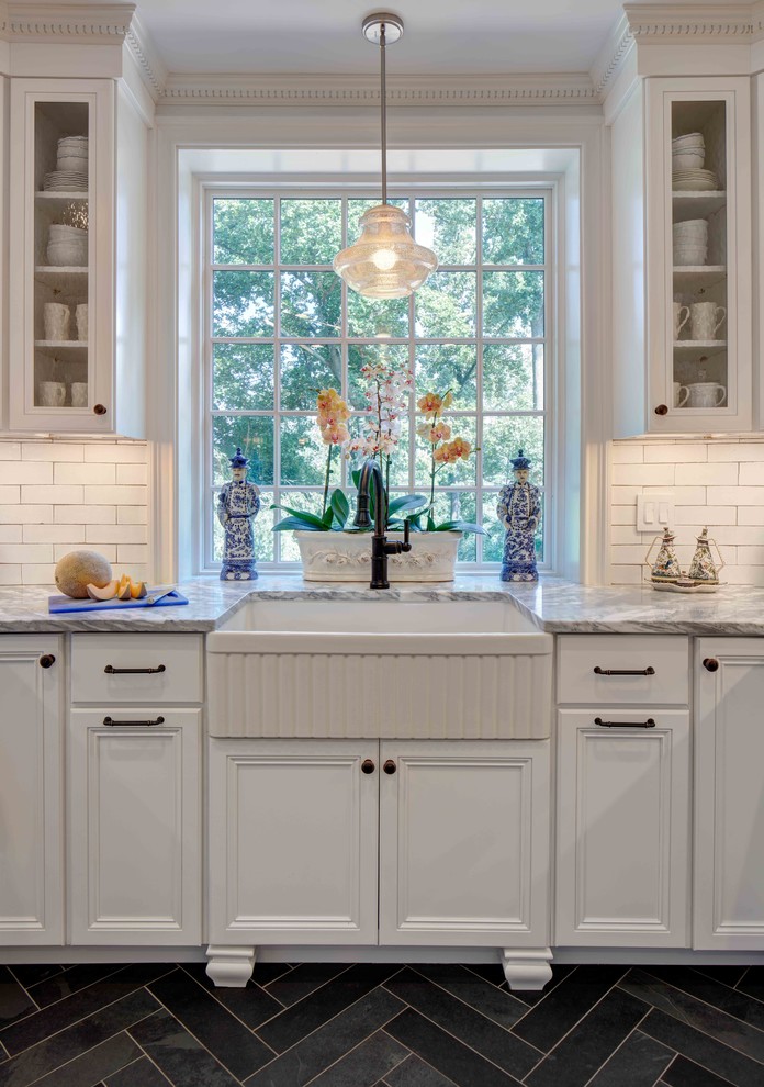 Inspiration for a mid-sized transitional u-shaped slate floor and gray floor eat-in kitchen remodel in New York with a farmhouse sink, recessed-panel cabinets, white cabinets, marble countertops, white backsplash, brick backsplash, paneled appliances and a peninsula