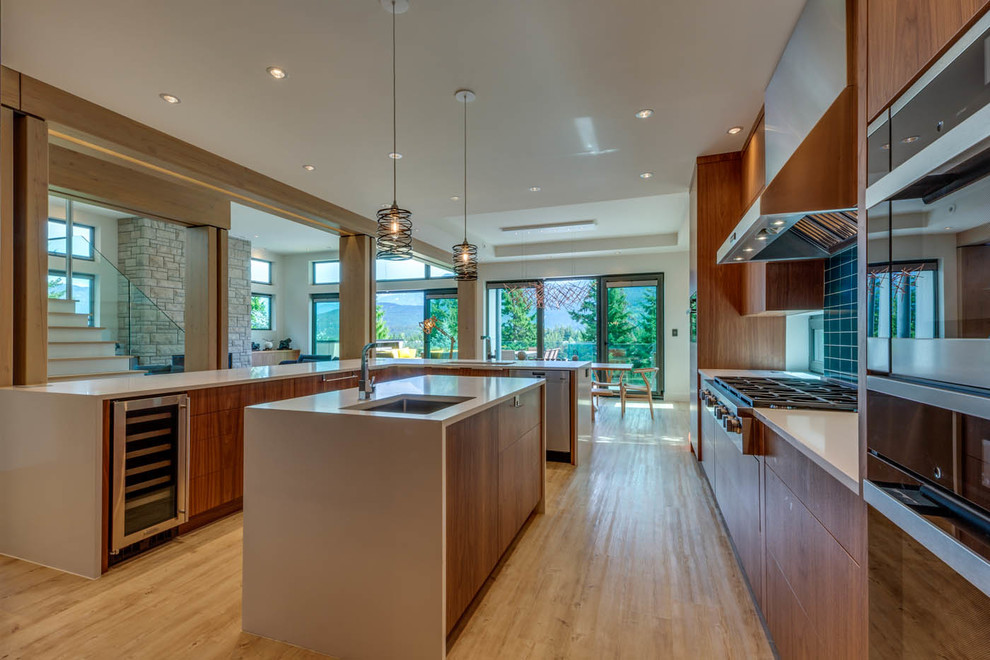 Photo of a large contemporary l-shaped open plan kitchen in Other with a submerged sink, flat-panel cabinets, dark wood cabinets, blue splashback, ceramic splashback, stainless steel appliances, light hardwood flooring, multiple islands and beige floors.