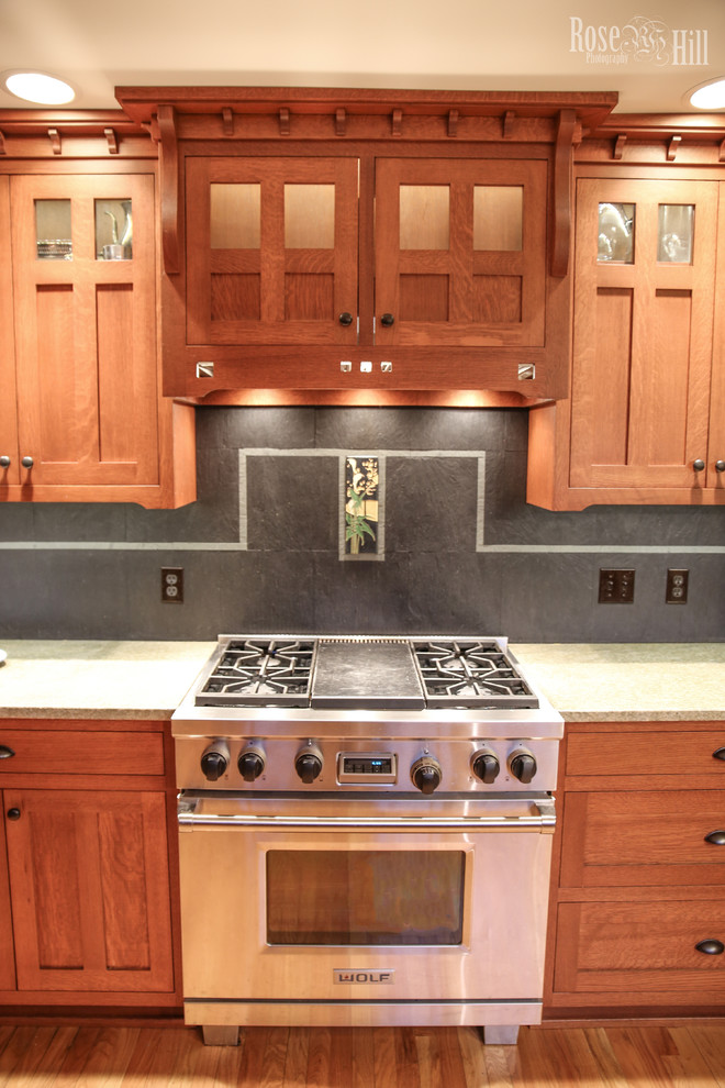 Photo of a medium sized traditional l-shaped kitchen/diner in Indianapolis with medium wood cabinets, granite worktops, glass-front cabinets, a breakfast bar, grey splashback, stone tiled splashback and stainless steel appliances.