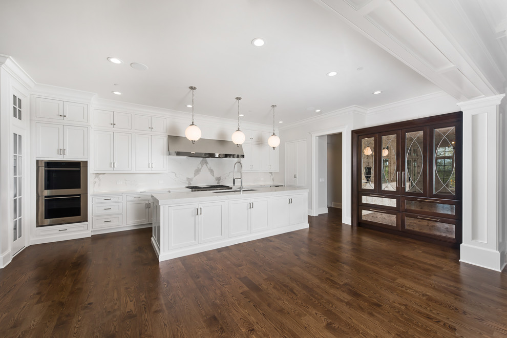 Inspiration för stora klassiska linjära vitt kök med öppen planlösning, med en undermonterad diskho, luckor med infälld panel, vita skåp, bänkskiva i kvarts, vitt stänkskydd, stänkskydd i sten, integrerade vitvaror, mörkt trägolv, en köksö och brunt golv