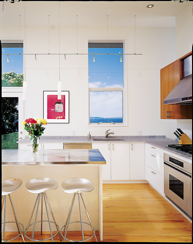Example of a trendy kitchen design in Seattle with an undermount sink, flat-panel cabinets, white cabinets, stainless steel countertops and stainless steel appliances