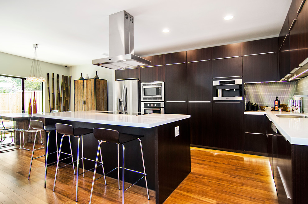 Ejemplo de cocina actual con armarios con paneles lisos, puertas de armario de madera en tonos medios, salpicadero gris y electrodomésticos de acero inoxidable