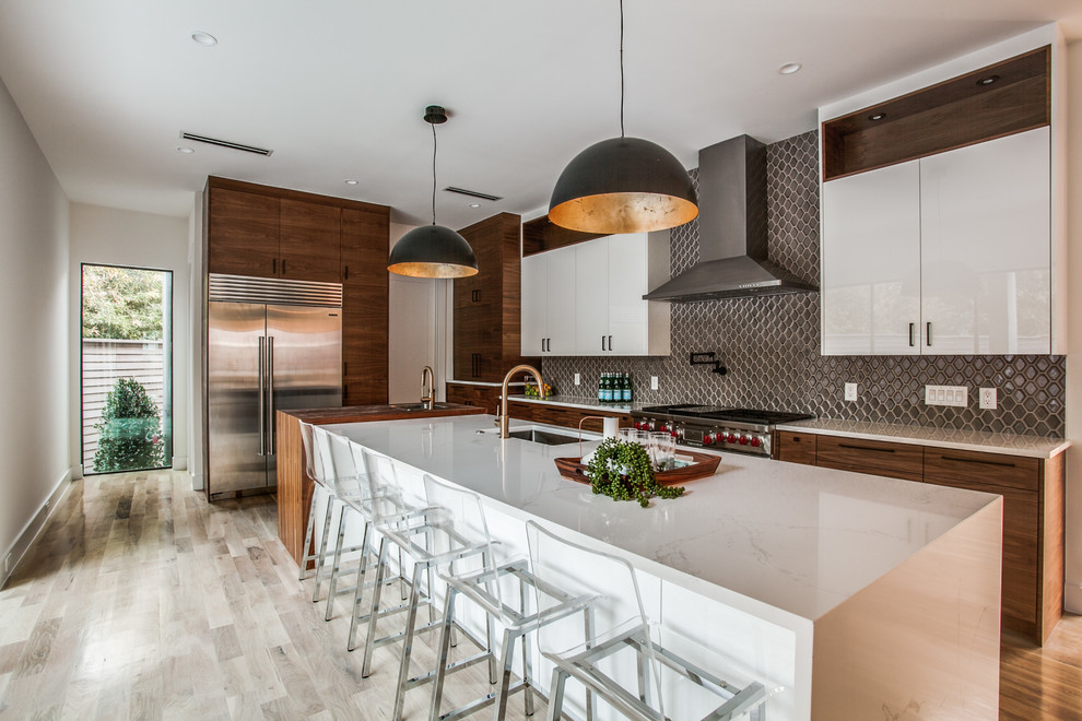 Large minimalist l-shaped medium tone wood floor and brown floor open concept kitchen photo in Dallas with a single-bowl sink, flat-panel cabinets, medium tone wood cabinets, quartzite countertops, gray backsplash, mosaic tile backsplash, stainless steel appliances and an island
