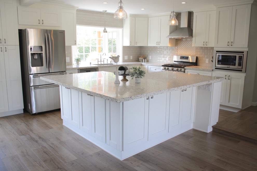 Example of a mid-sized transitional l-shaped medium tone wood floor open concept kitchen design in Los Angeles with an undermount sink, shaker cabinets, white cabinets, granite countertops, white backsplash, subway tile backsplash, stainless steel appliances and an island