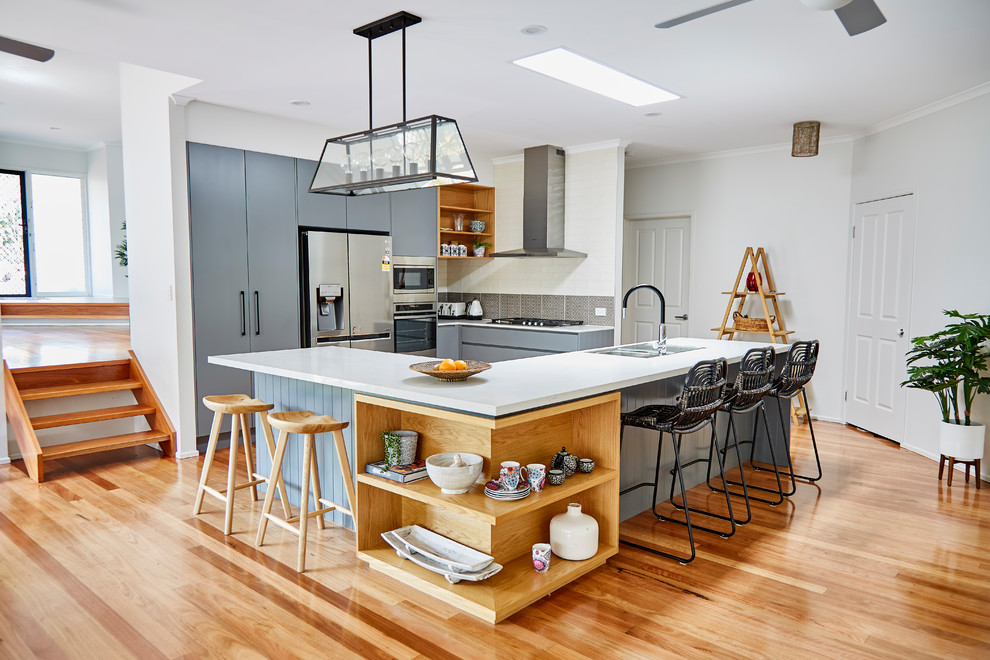 Offene Moderne Küche in U-Form mit flächenbündigen Schrankfronten, grauen Schränken, Küchenrückwand in Grau, Küchengeräten aus Edelstahl, hellem Holzboden, Kücheninsel und braunem Boden in Sonstige