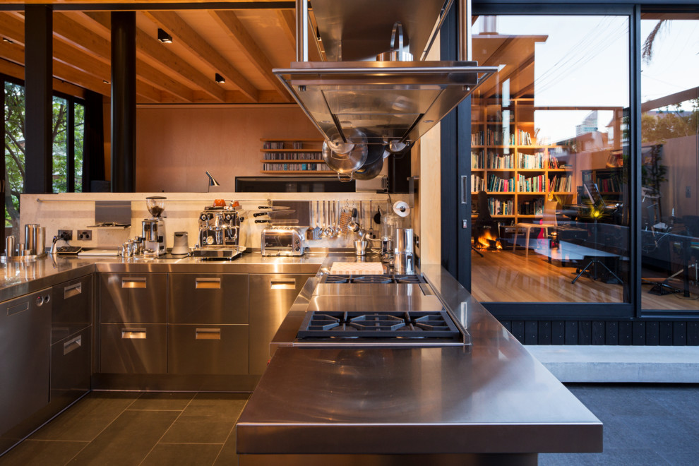 Example of a large trendy u-shaped slate floor eat-in kitchen design in Auckland with an integrated sink, flat-panel cabinets, stainless steel cabinets, stainless steel countertops, stainless steel appliances and an island