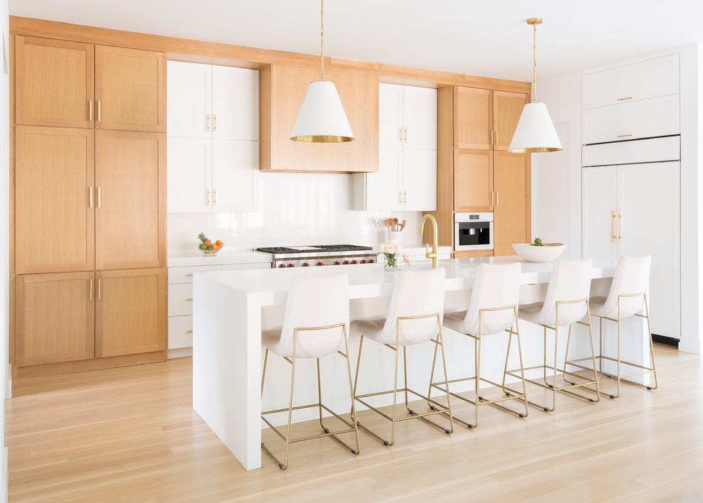 ダラスにある高級な中くらいなコンテンポラリースタイルのおしゃれなキッチン (アンダーカウンターシンク、シェーカースタイル扉のキャビネット、中間色木目調キャビネット、白いキッチンパネル、石スラブのキッチンパネル、パネルと同色の調理設備、淡色無垢フローリング、ベージュの床、白いキッチンカウンター、人工大理石カウンター) の写真