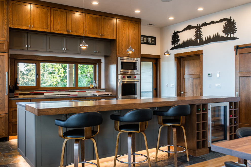 Aménagement d'une cuisine parallèle montagne en bois brun avec un placard à porte shaker, un électroménager en acier inoxydable, îlot, un sol marron et un plan de travail gris.