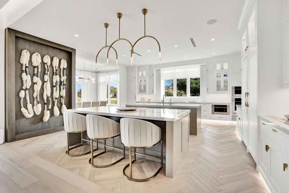 Design ideas for an expansive contemporary l-shaped open plan kitchen in Miami with a submerged sink, shaker cabinets, white cabinets, marble worktops, white splashback, marble splashback, stainless steel appliances, medium hardwood flooring, multiple islands, beige floors and white worktops.