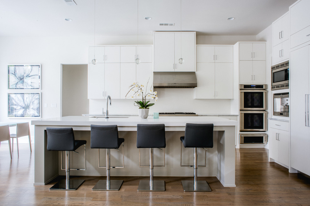 Zweizeilige Moderne Küche mit flächenbündigen Schrankfronten, weißen Schränken, Küchenrückwand in Weiß, Küchengeräten aus Edelstahl, Kücheninsel und dunklem Holzboden in Dallas