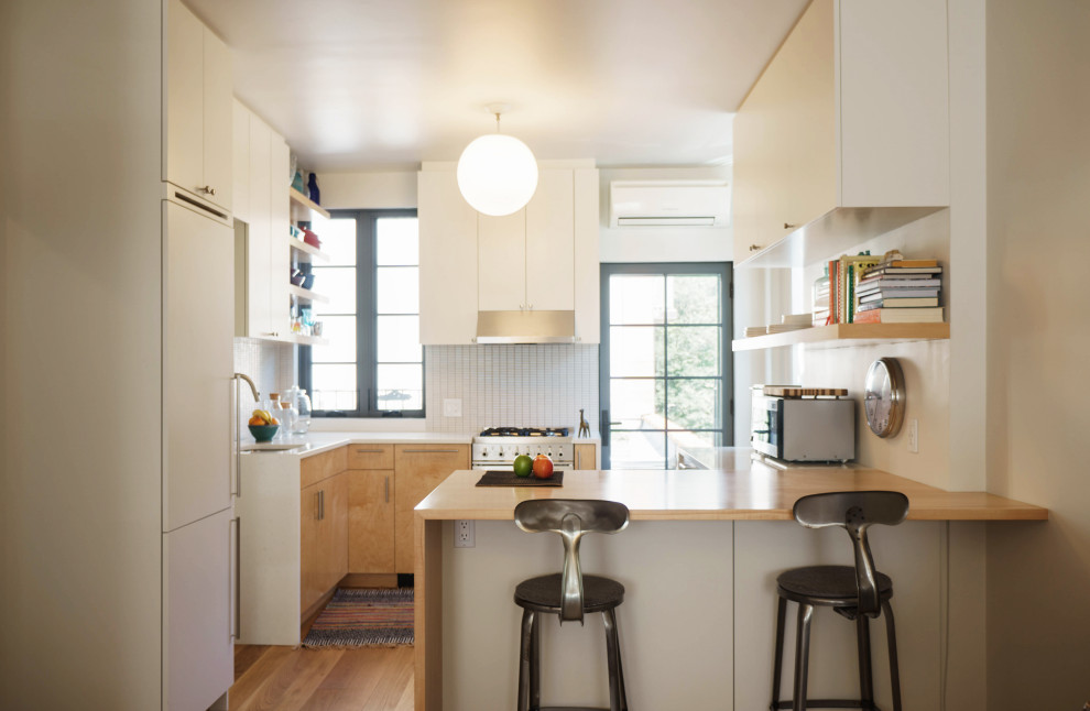Mid-sized trendy l-shaped medium tone wood floor eat-in kitchen photo in New York with an undermount sink, flat-panel cabinets, light wood cabinets, quartzite countertops, white backsplash, mosaic tile backsplash, stainless steel appliances, an island and white countertops