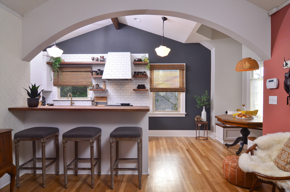 Foto på ett litet vintage brun kök, med vita skåp, träbänkskiva, vitt stänkskydd, stänkskydd i tunnelbanekakel, mellanmörkt trägolv, en halv köksö och brunt golv