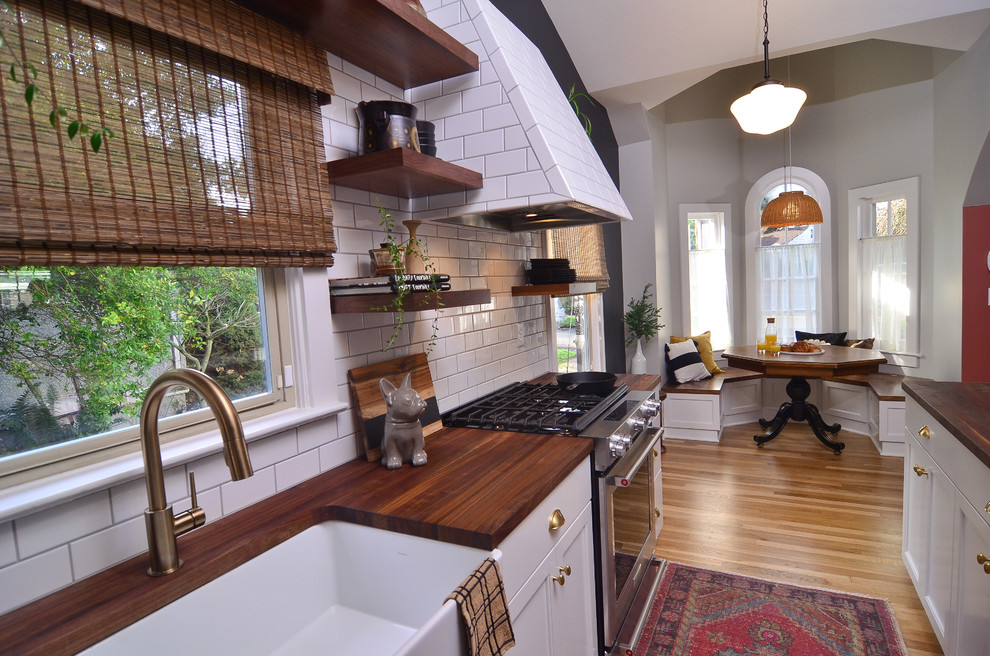 Eat-in kitchen - small transitional galley medium tone wood floor and brown floor eat-in kitchen idea in Portland with a farmhouse sink, recessed-panel cabinets, white cabinets, wood countertops, white backsplash, subway tile backsplash, stainless steel appliances, a peninsula and brown countertops