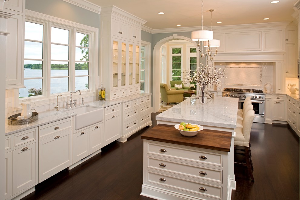 Inspiration for a large timeless u-shaped dark wood floor and brown floor enclosed kitchen remodel in Minneapolis with a farmhouse sink, marble countertops, white cabinets, white backsplash, subway tile backsplash, stainless steel appliances, an island, white countertops and recessed-panel cabinets