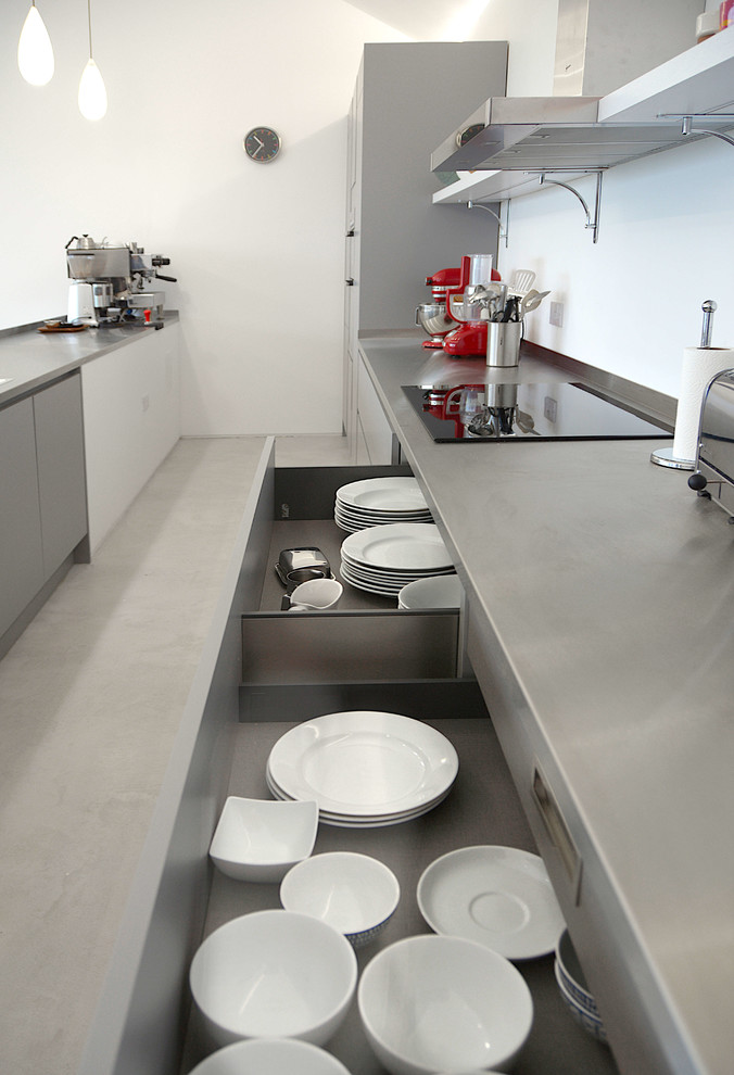 Medium sized contemporary galley open plan kitchen in Cornwall with flat-panel cabinets, grey cabinets, stainless steel worktops and concrete flooring.