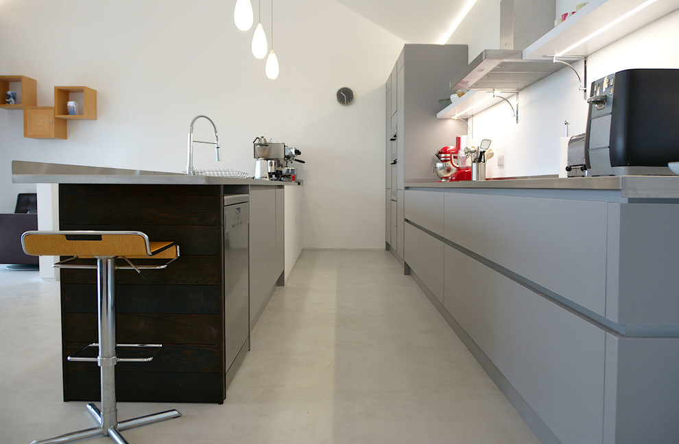 Offene, Zweizeilige, Mittelgroße Moderne Küche mit flächenbündigen Schrankfronten, grauen Schränken, Edelstahl-Arbeitsplatte und Betonboden in Cornwall