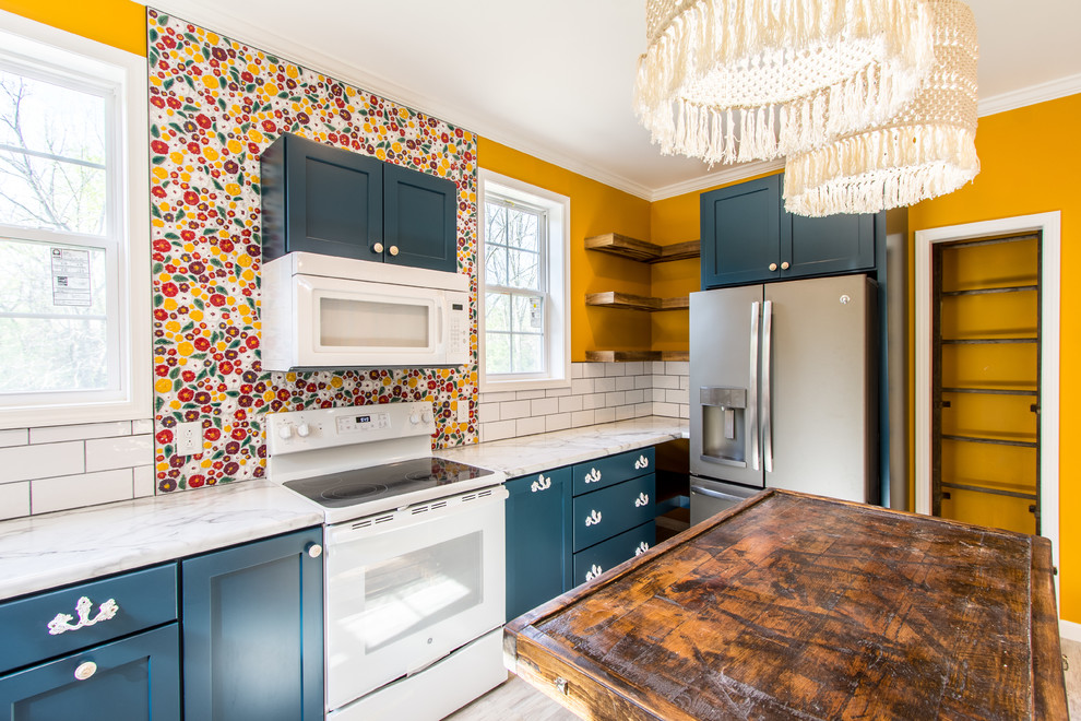 Inspiration for a mid-sized shabby-chic style l-shaped laminate floor and gray floor eat-in kitchen remodel in Other with a farmhouse sink, flat-panel cabinets, blue cabinets, laminate countertops, white backsplash, ceramic backsplash, white appliances, an island and white countertops