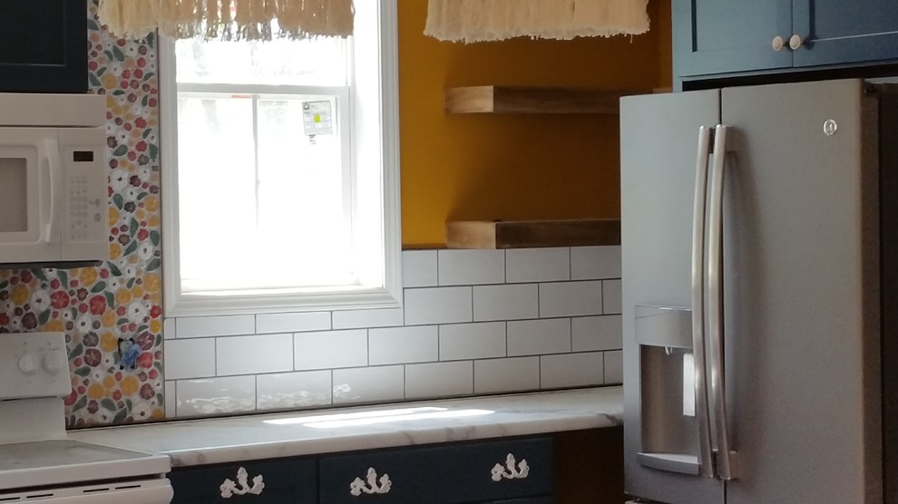 Photo of a medium sized shabby-chic style l-shaped kitchen/diner in Other with a belfast sink, flat-panel cabinets, blue cabinets, laminate countertops, white splashback, ceramic splashback, white appliances, laminate floors, an island, grey floors and white worktops.