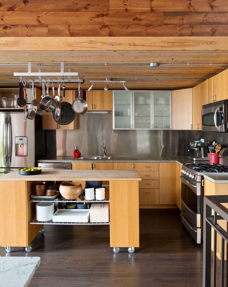 This is an example of an industrial l-shaped open plan kitchen in Toronto with a double-bowl sink, flat-panel cabinets, light wood cabinets, concrete worktops, metallic splashback, stainless steel appliances, dark hardwood flooring, an island and brown floors.