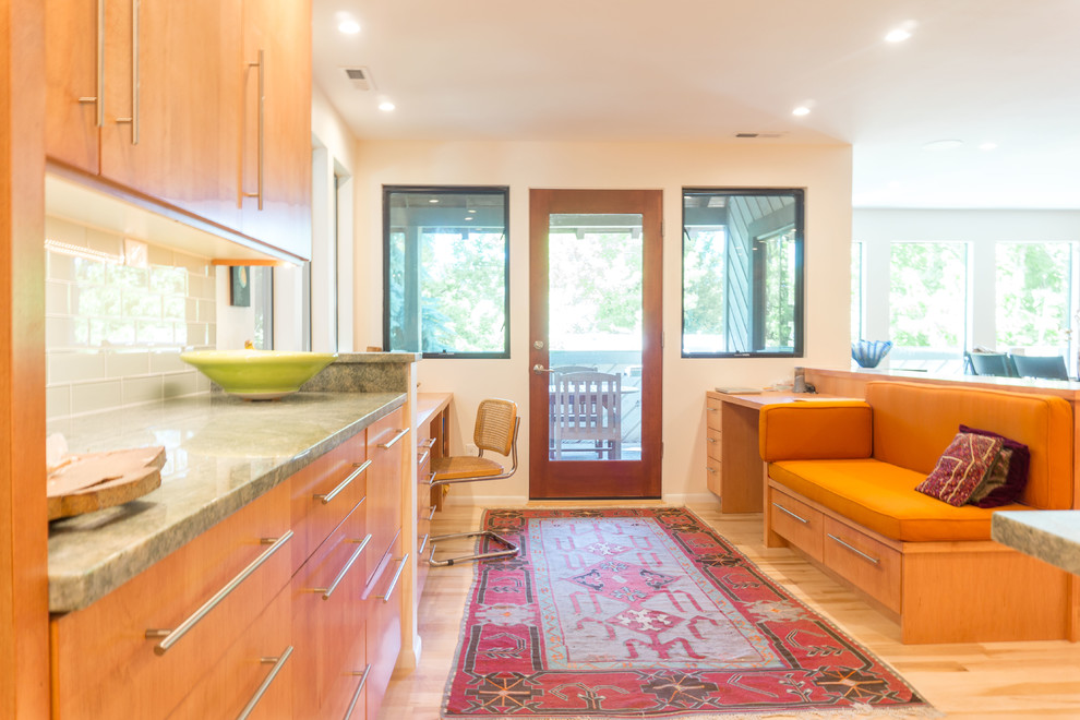 Foto på ett mellanstort funkis kök, med en undermonterad diskho, släta luckor, skåp i mellenmörkt trä, granitbänkskiva, grönt stänkskydd, stänkskydd i glaskakel, svarta vitvaror, ljust trägolv och en köksö