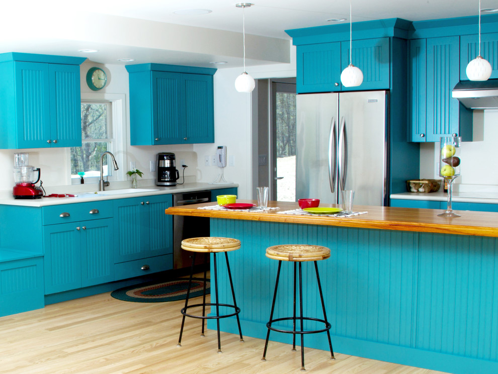 Photo of a medium sized eclectic l-shaped kitchen/diner in Milwaukee with an integrated sink, turquoise cabinets, wood worktops, white splashback, stainless steel appliances, light hardwood flooring, an island, flat-panel cabinets, brown floors and white worktops.