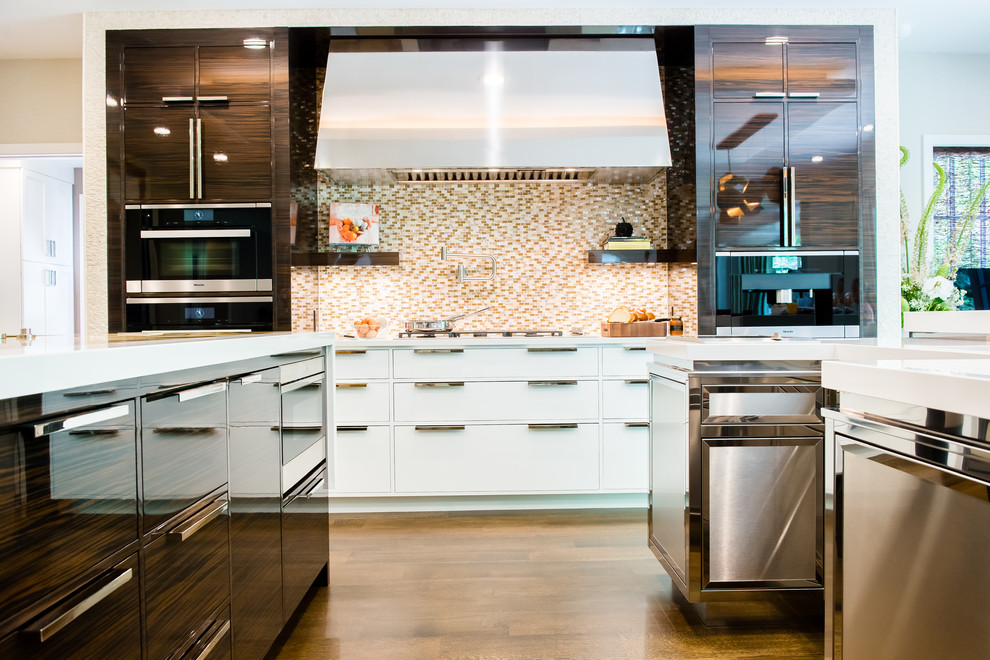 Bild på ett stort funkis kök, med en enkel diskho, släta luckor, skåp i rostfritt stål, bänkskiva i kvartsit, integrerade vitvaror, mellanmörkt trägolv, flera köksöar, beige stänkskydd och stänkskydd i stenkakel