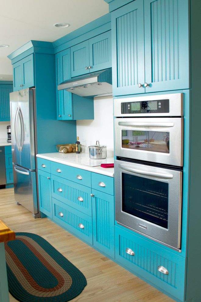 Design ideas for a medium sized bohemian l-shaped kitchen/diner in Milwaukee with turquoise cabinets, white splashback, stainless steel appliances, light hardwood flooring, an island, a single-bowl sink, flat-panel cabinets, yellow floors and white worktops.
