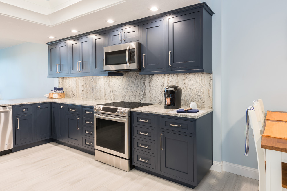 Inspiration for a large transitional l-shaped porcelain tile and white floor eat-in kitchen remodel in Orlando with an undermount sink, blue cabinets, granite countertops, beige backsplash, stone slab backsplash, stainless steel appliances, a peninsula and beige countertops