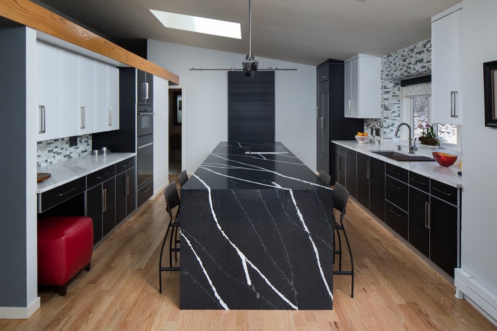 Inspiration för stora moderna svart kök, med en undermonterad diskho, släta luckor, svarta skåp, bänkskiva i kvarts, flerfärgad stänkskydd, stänkskydd i glaskakel, integrerade vitvaror, ljust trägolv, en köksö och beiget golv