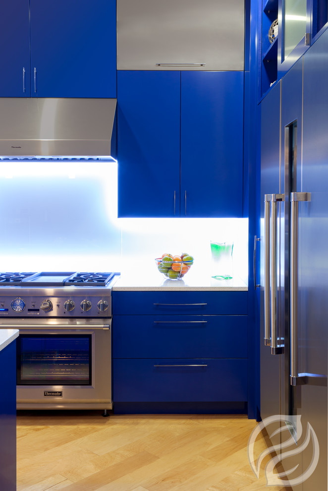 Ispirazione per una cucina minimal chiusa e di medie dimensioni con ante lisce, ante blu, top in quarzo composito, paraspruzzi bianco, paraspruzzi con lastra di vetro, elettrodomestici in acciaio inossidabile e parquet chiaro