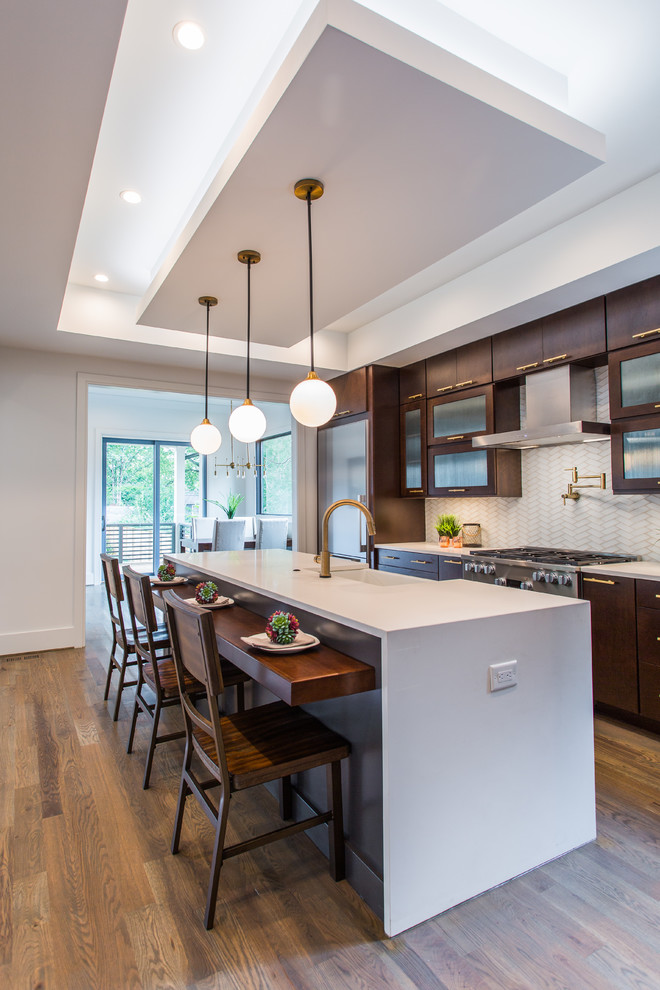 Design ideas for a large modern l-shaped kitchen/diner in Charlotte with a belfast sink, flat-panel cabinets, dark wood cabinets, engineered stone countertops, beige splashback, stainless steel appliances, medium hardwood flooring, an island and brown floors.