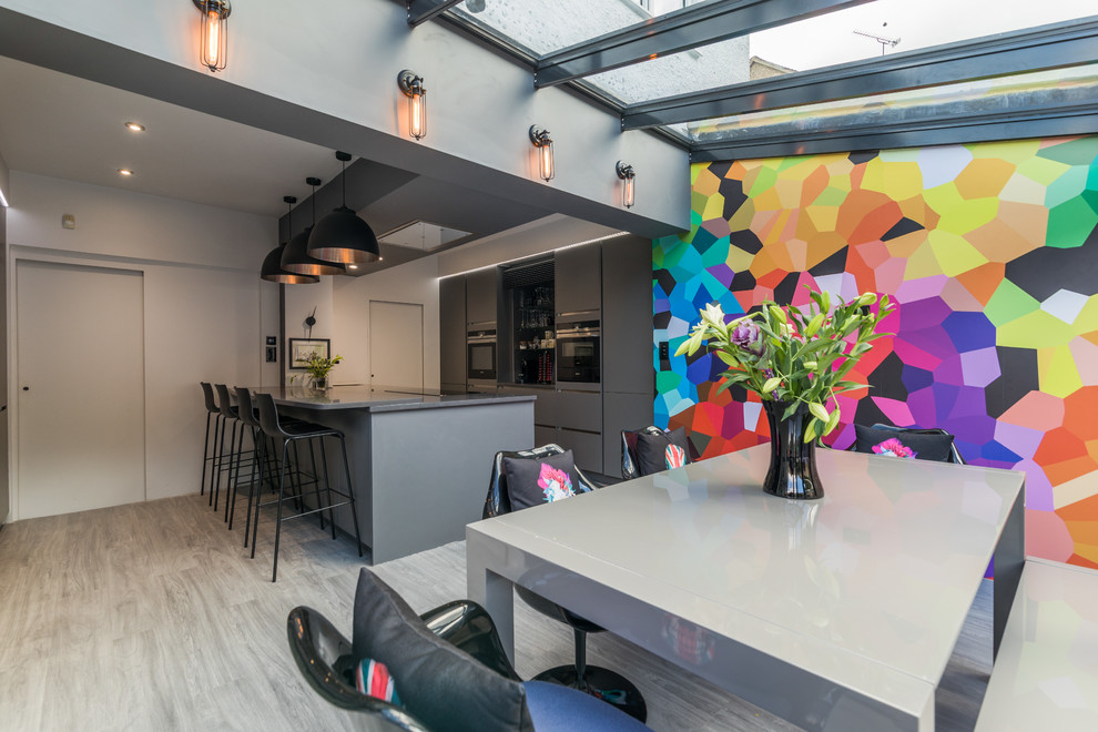 Example of a mid-sized trendy galley gray floor and light wood floor eat-in kitchen design in London with flat-panel cabinets, gray cabinets, an island and stainless steel appliances