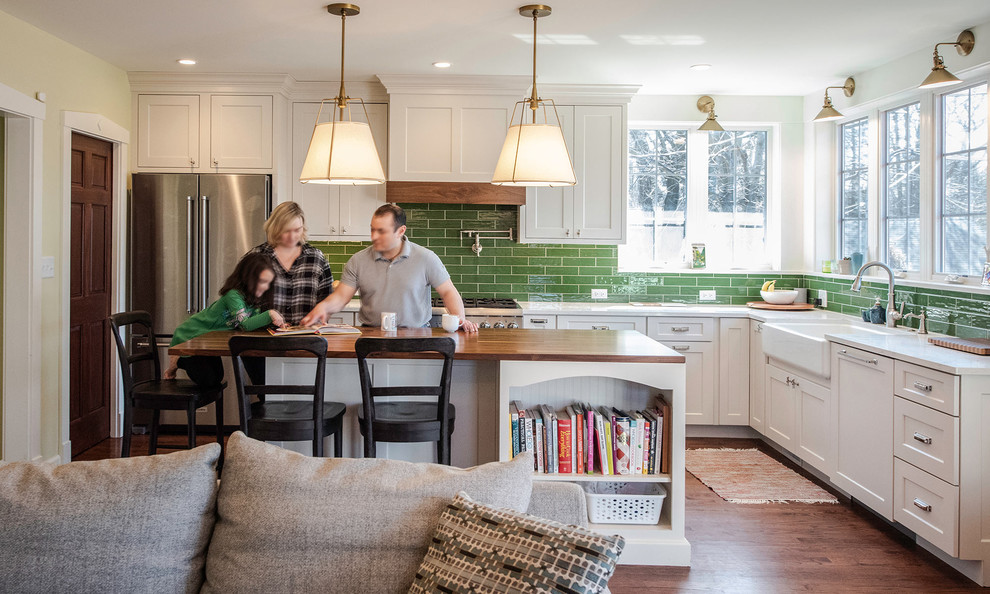 Mid-sized elegant l-shaped brown floor and medium tone wood floor open concept kitchen photo in Other with a farmhouse sink, white cabinets, granite countertops, green backsplash, stainless steel appliances, an island, white countertops, shaker cabinets and subway tile backsplash