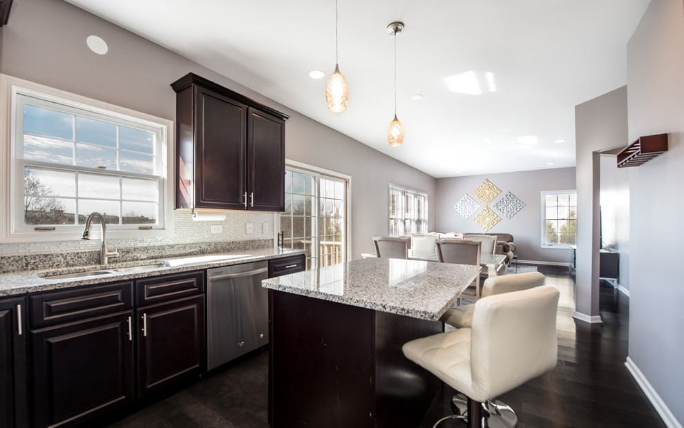 Medium sized traditional l-shaped open plan kitchen in Chicago with a double-bowl sink, raised-panel cabinets, dark wood cabinets, recycled glass countertops, stainless steel appliances, dark hardwood flooring, an island, brown floors, metallic splashback, glass sheet splashback and grey worktops.