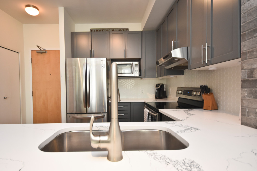 This is an example of a medium sized industrial u-shaped kitchen/diner in Ottawa with a submerged sink, shaker cabinets, grey cabinets, engineered stone countertops, white splashback, porcelain splashback, stainless steel appliances, laminate floors and white worktops.