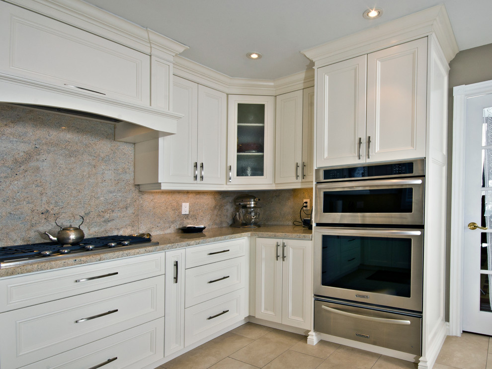 Klassisk inredning av ett mellanstort kök, med en undermonterad diskho, vita skåp, granitbänkskiva, flerfärgad stänkskydd, stänkskydd i sten, rostfria vitvaror, klinkergolv i porslin, luckor med infälld panel, en halv köksö och beiget golv