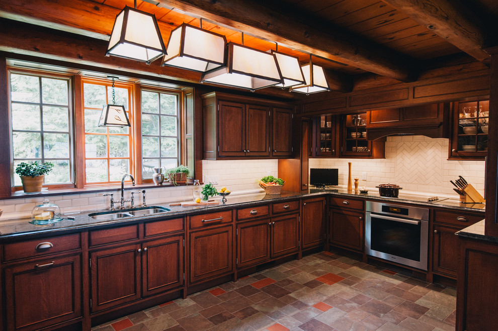 Foto på ett stort rustikt kök, med luckor med profilerade fronter, skåp i mörkt trä, granitbänkskiva, vitt stänkskydd, stänkskydd i tunnelbanekakel, rostfria vitvaror, en dubbel diskho och skiffergolv