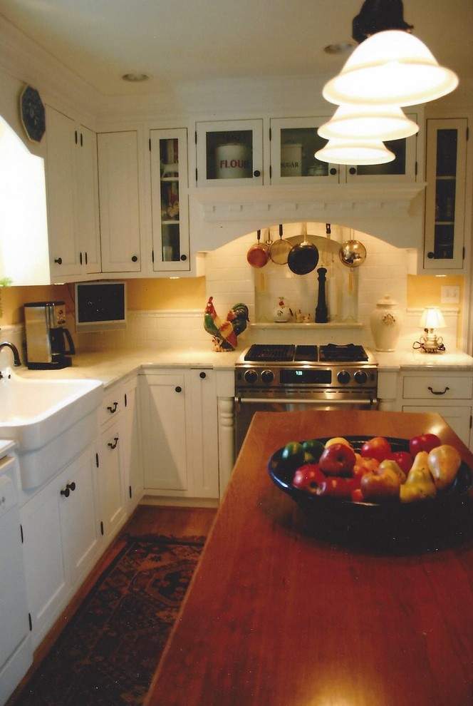 Lantlig inredning av ett mellanstort l-kök, med en rustik diskho, skåp i shakerstil, vita skåp, träbänkskiva, vitt stänkskydd, stänkskydd i tunnelbanekakel, rostfria vitvaror, mellanmörkt trägolv och en köksö