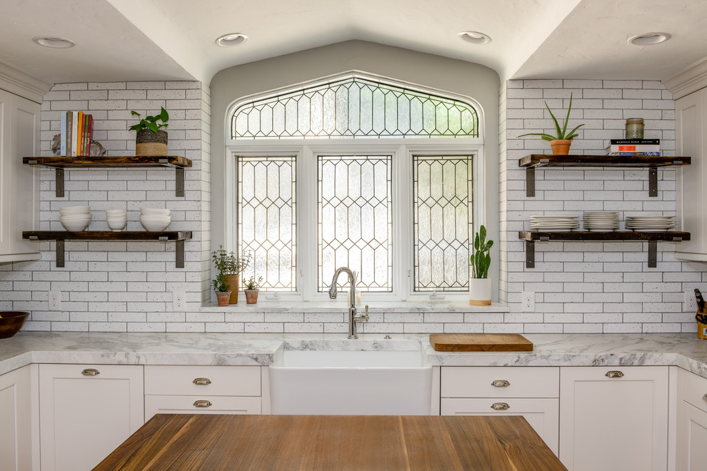 Mid-sized eclectic u-shaped medium tone wood floor and brown floor enclosed kitchen photo in Denver with a farmhouse sink, flat-panel cabinets, white cabinets, quartzite countertops, white backsplash, brick backsplash, paneled appliances, an island and white countertops